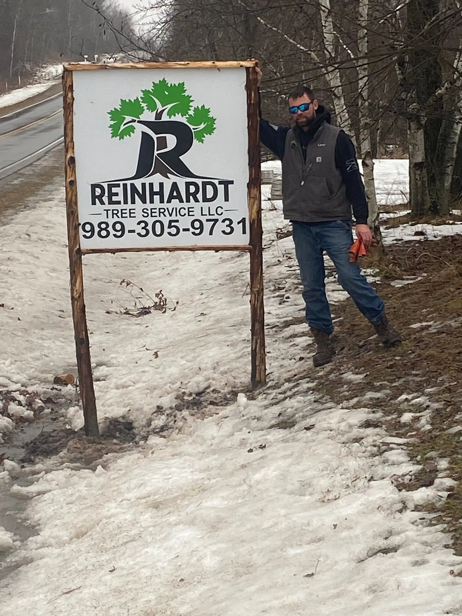 Larry Reinhardt beside the Reinhardt Tree Service roadside sign